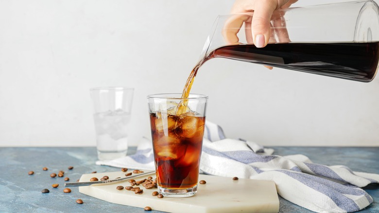 Cold brew being poured from a pitcher into a glass with ice