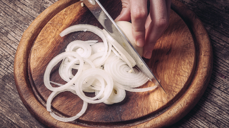 Slicing white onion on wooden cutting board