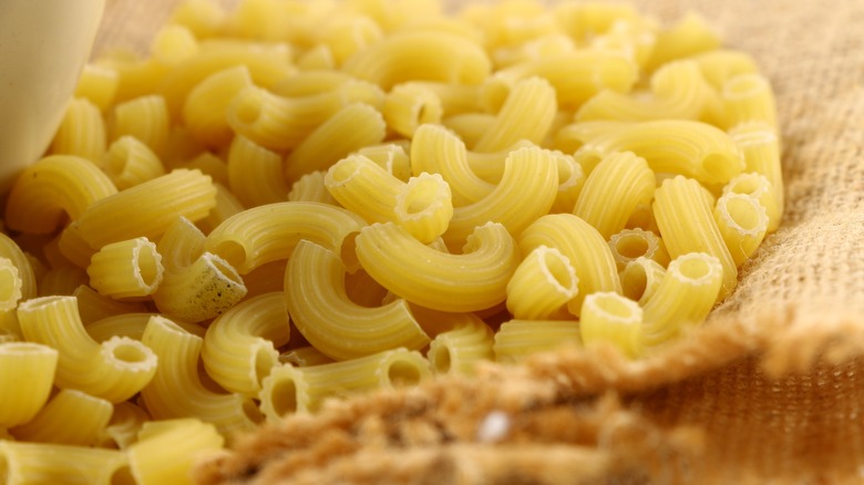 Dry macaroni noodles sitting on a burlap bag.