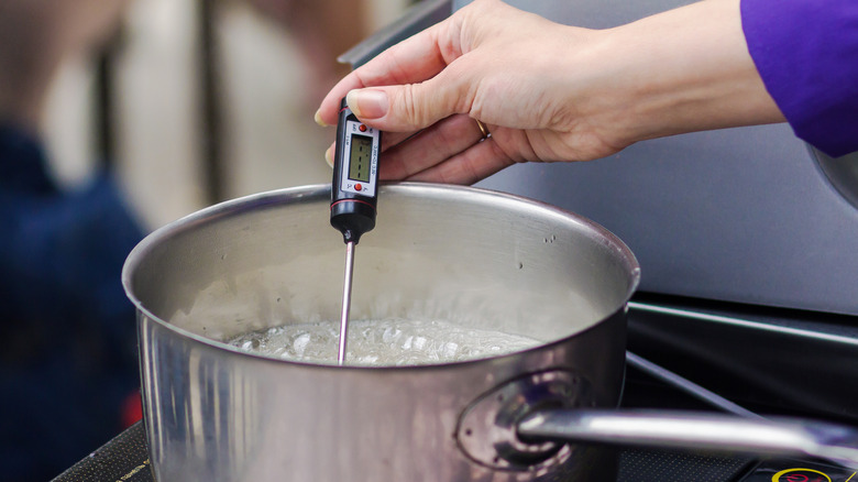Hand holding candy thermometer in hot sugar
