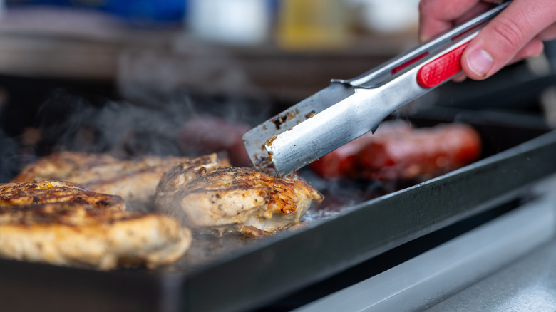Seasoned chicken and sausages cooking on a Blackstone griddle