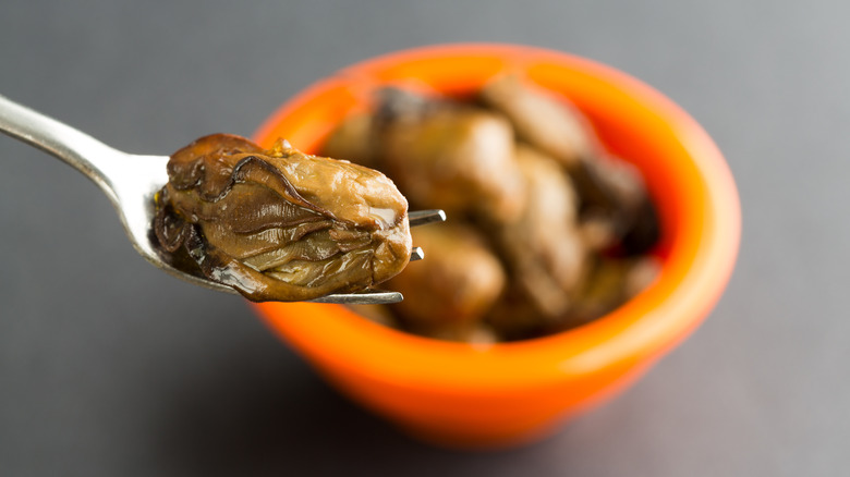 Fork holding up canned oyster in front of bowl