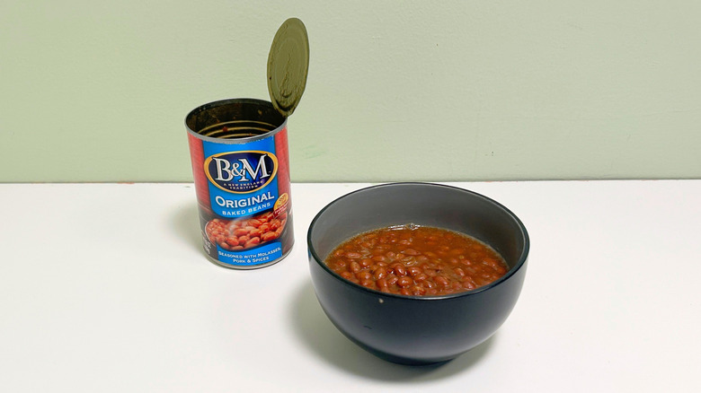 A black bowl of baked beans next to an open can of B&M Original Baked Beans