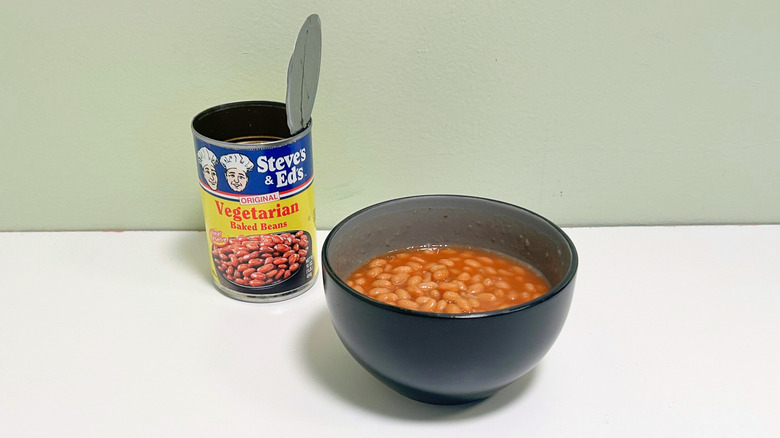 A black bowl of baked beans next to an open can of Steve's and Ed's Vegetarian Baked Beans