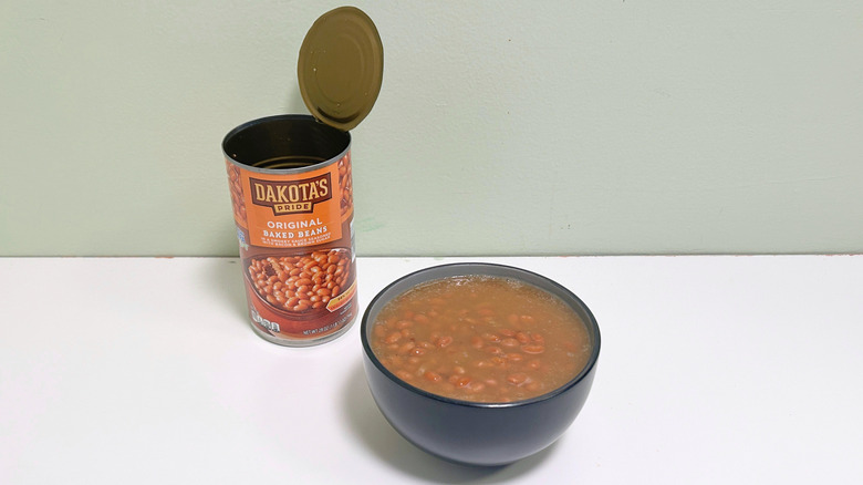 A black bowl of baked beans next to an open can of Dakota's Pride Original Baked Beans