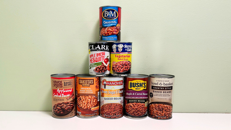 Eight cans of baked beans from various brands arranged in a pyramid