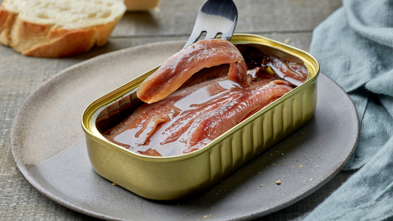 A fork lifts an anchovy fillet out of a can