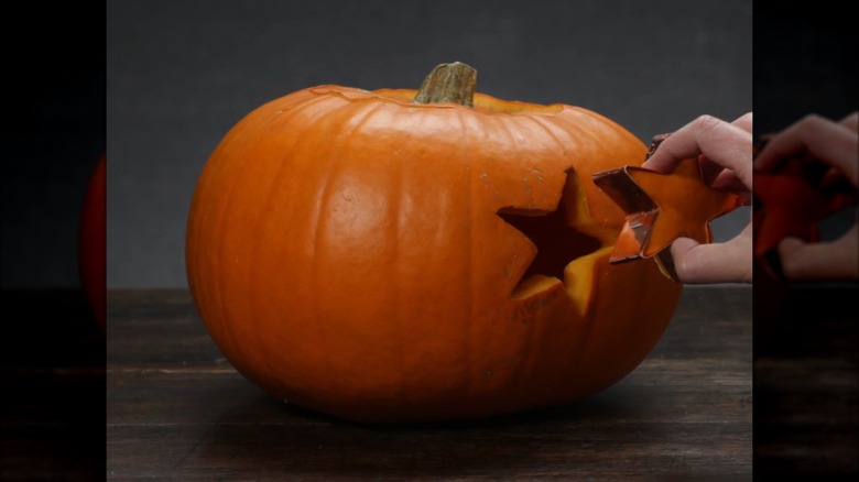 Hand pulling star cookie cutter and pumpkin flesh away from pumpking