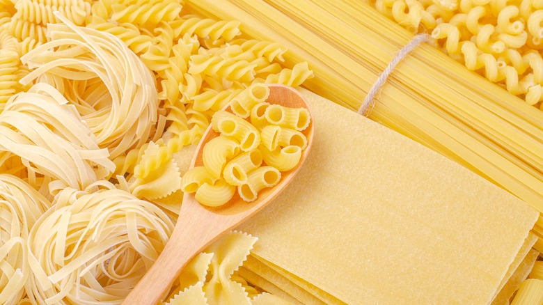 Various dried pasta shapes with wooden spoon