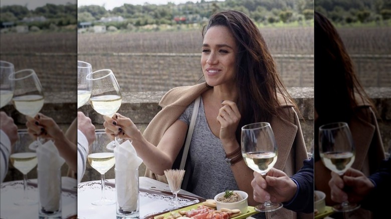 Meghan Markle toasting with wine at an outdoor table at a vineyard