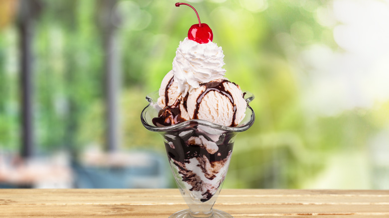 Hot fudge sundae on a table outside with a cherry on top