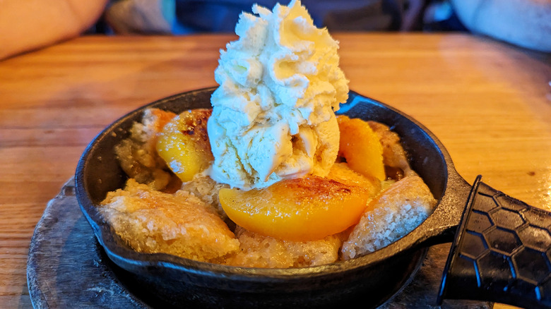 Peach cobbler with whipped cream in cast iron skillet