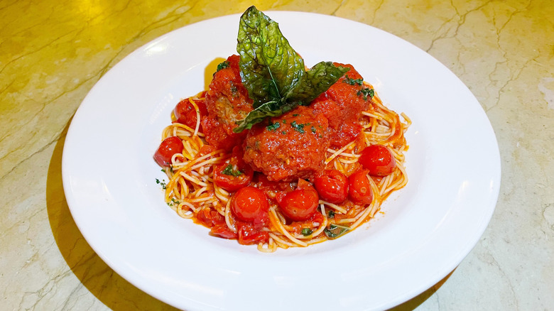 A bowl of spaghetti and meatballs garnished with tall fried basil leaves