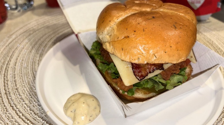 A plate with an Original Jalapeño Ranch Club Chicken Sandwich its its box with sauce on the side