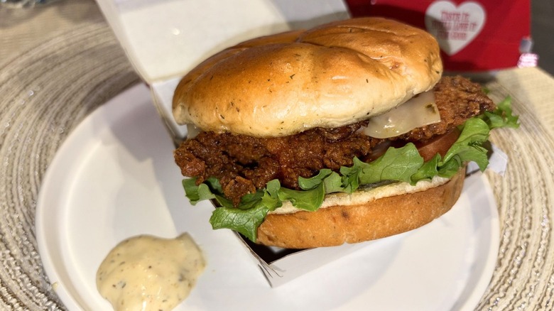 A plate with a Spicy Jalapeño Ranch Club Chicken Sandwich and its box with sauce on the side