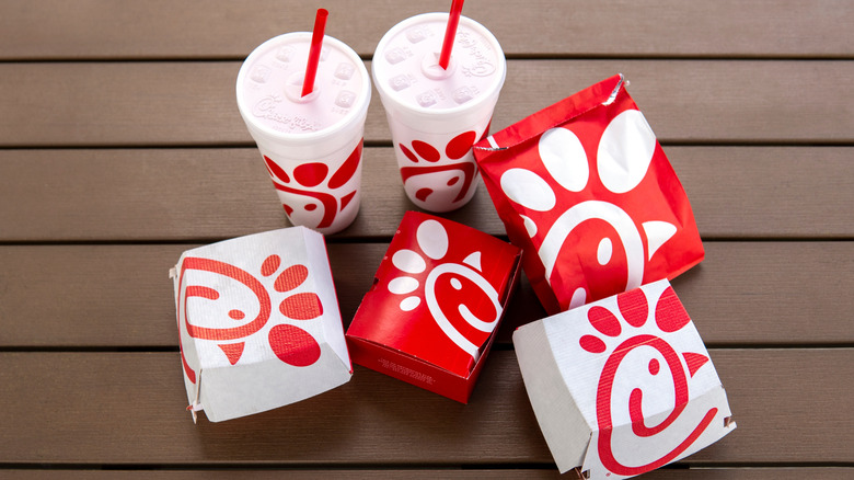 Red and white Chick-fil-A takeout containers and cups on a brown wooden table