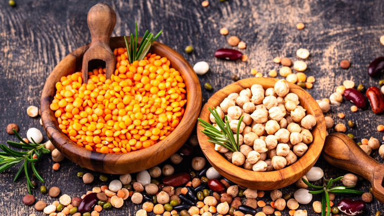 Bowls of dry chickpeas and red lentils, surrounded by miscellaneous legumes.