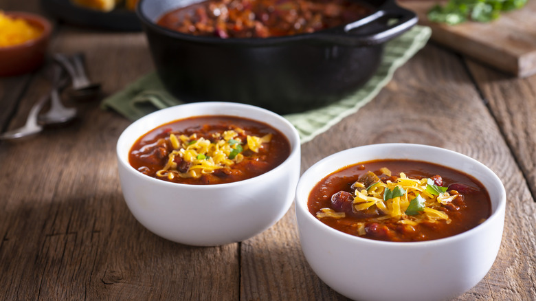 Two bowls of homemade chili with a pot in the background and cornbread