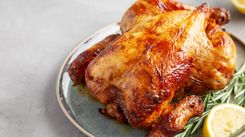 Rotisserie chicken on plate with tight skin, lemon, and herbs