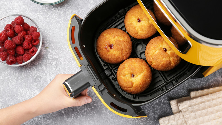 A person pulling out an air fryer drawer with muffins in it