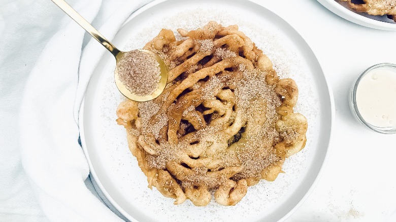 sprinkling cinnamon sugar on funnel cake