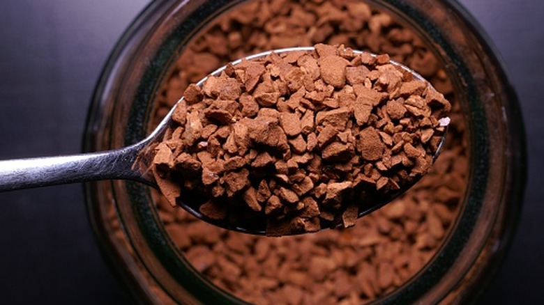 A close-up of a spoonful of freeze-dried instant coffee over the mouth of the jar
