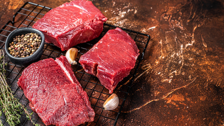 Slabs of raw venison on a wire rack with herbs, garlic, and peppercorns