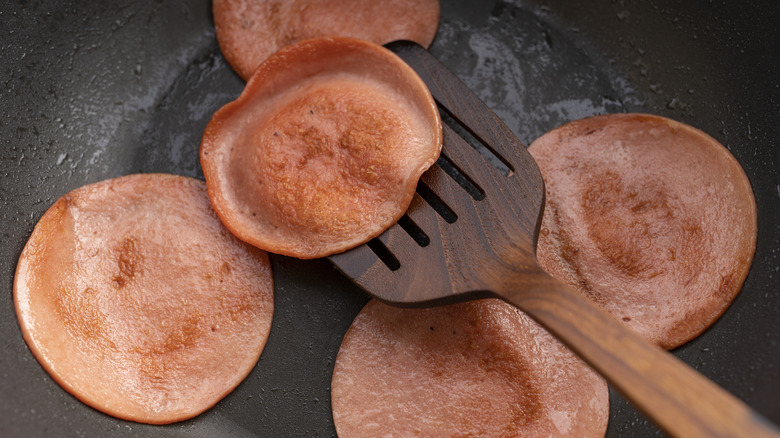 Bologna frying in pan with wooden spatula