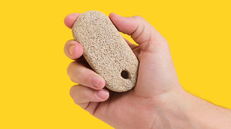 hand holding pumice stone against yellow background