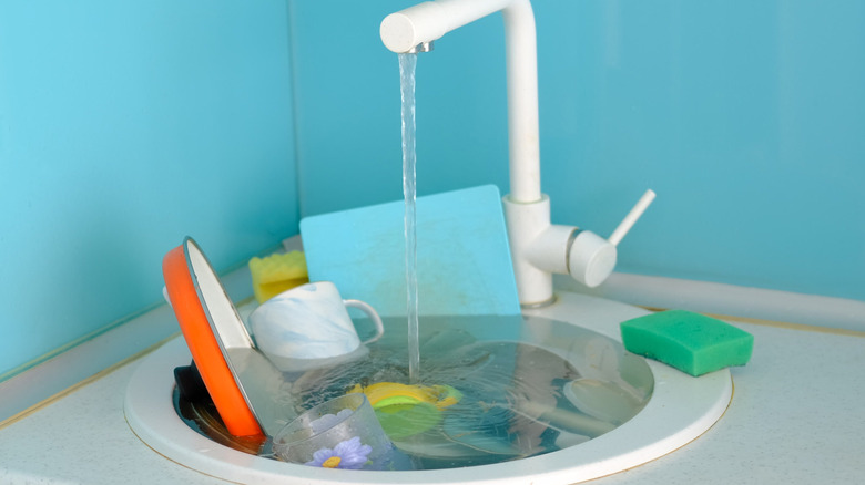A sink full of water and dishes with a white faucet and blue background