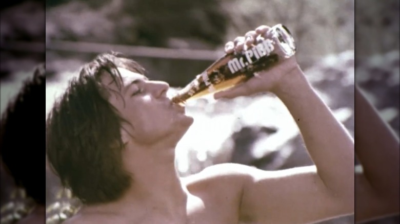 A vintage ad showing a young man drinking a glass Mr. PiBB bottle in the sun