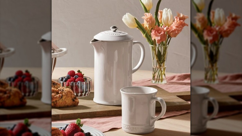A white french press made of stoneware with complementary mug