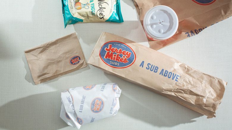 A Jersey Mike's sub, side, drink, and chips on a white table