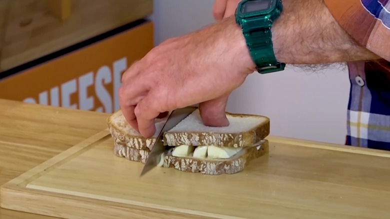 A man cuts a banana and mayo sandwich in half