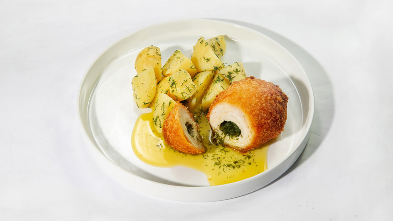 A chicken kiev on a plate, with boiled potatoes