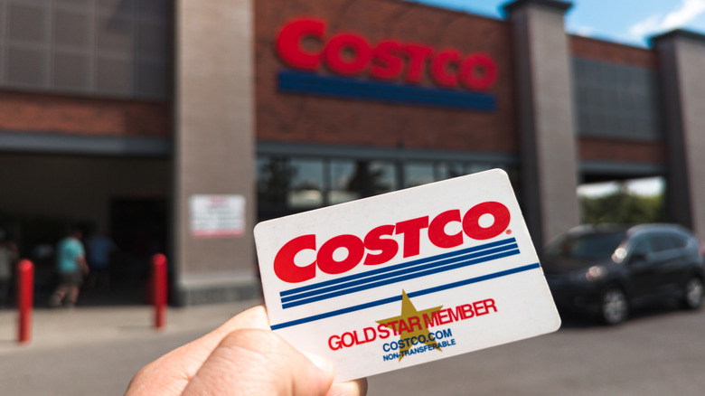 Hand holding Costco membership card in front of warehouse