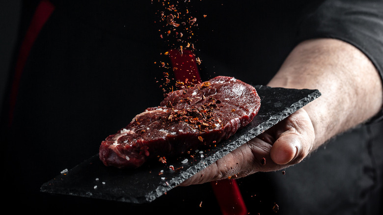 A piece of meat being generously seasoned