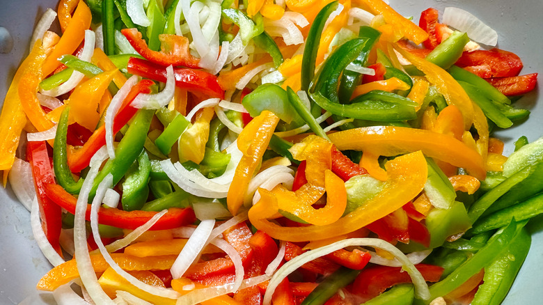 Red, yellow, and green peppers with onions cooking in a pan