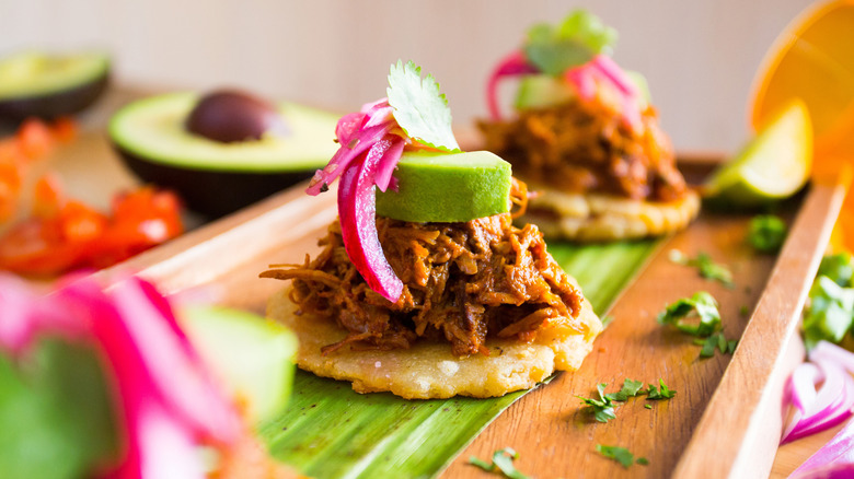 a canapé-sized tostada with carnitas, pickled red onion, avocado, and cilantro on top in an elegant presenation