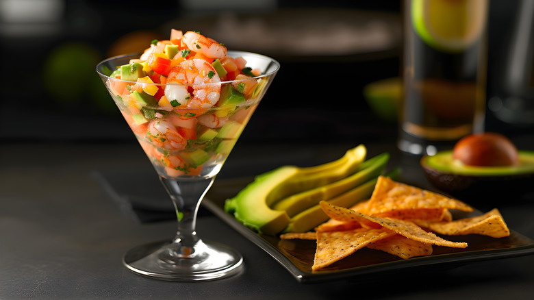 Shrimp and avocado ceviche in a martini glass with a plate of tortilla chips and slices of avocado