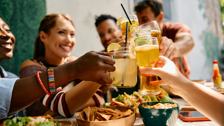 People smiling and toasting with different Mexican beers and cocktails at a table with tortilla chips, salad, and tacos