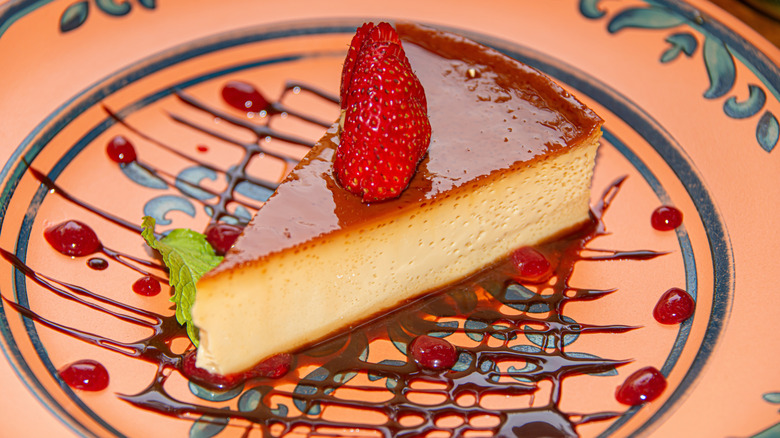 a slice of chocolate-covered flan garnished with strawberry and a mint leaf with chocolate drizzle