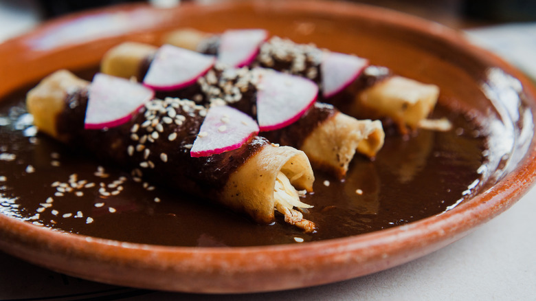 Ahicken enchiladas in a dark mole sauce, garnished with radishes and seeds