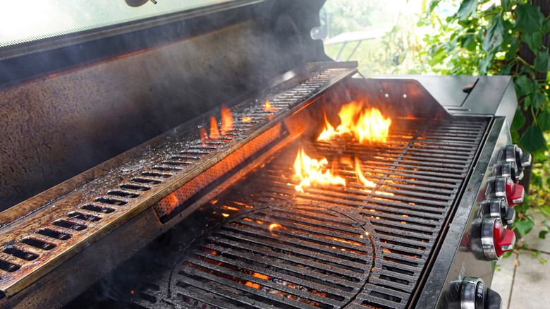 A greasy gas grill with the grates themselves in the flames