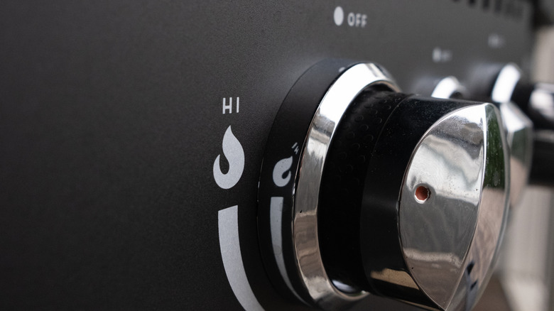 Closeup of a black plastic knob on a gas grill, controlling burner strength