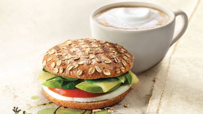 A Panera Bread Avocado, Egg White & Spinach on Sprouted Grain Bagel Flat sandwich with a cappuccino