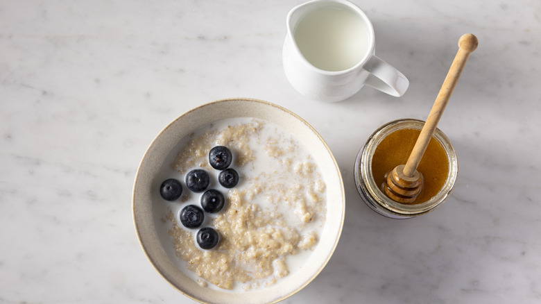 Bowl of oatmeal with blueberries, honey and milk on the side