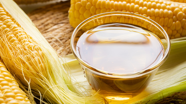 Corn silk tea in a cup alongside fresh corn.
