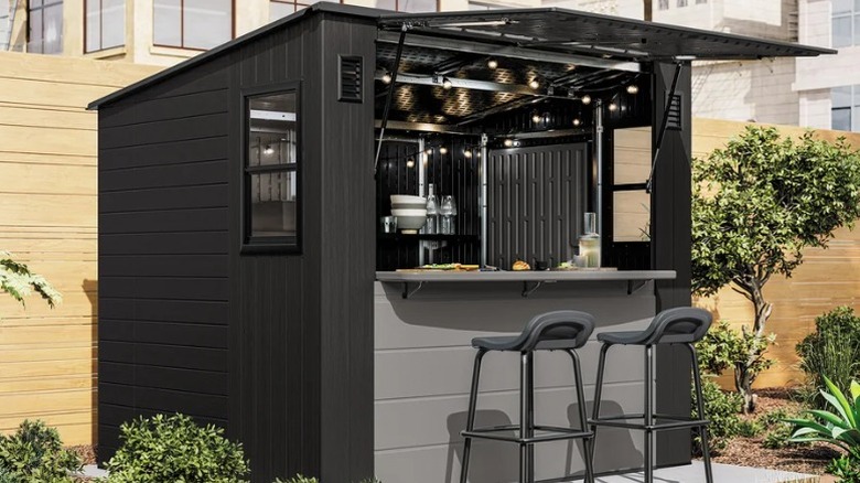 a gray shed in a backyard with open canopy and two barstools at the front