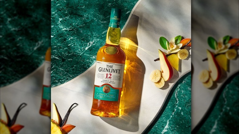 a bottle of scotch with a turqouise background surrounded by flowers and sliced fruits